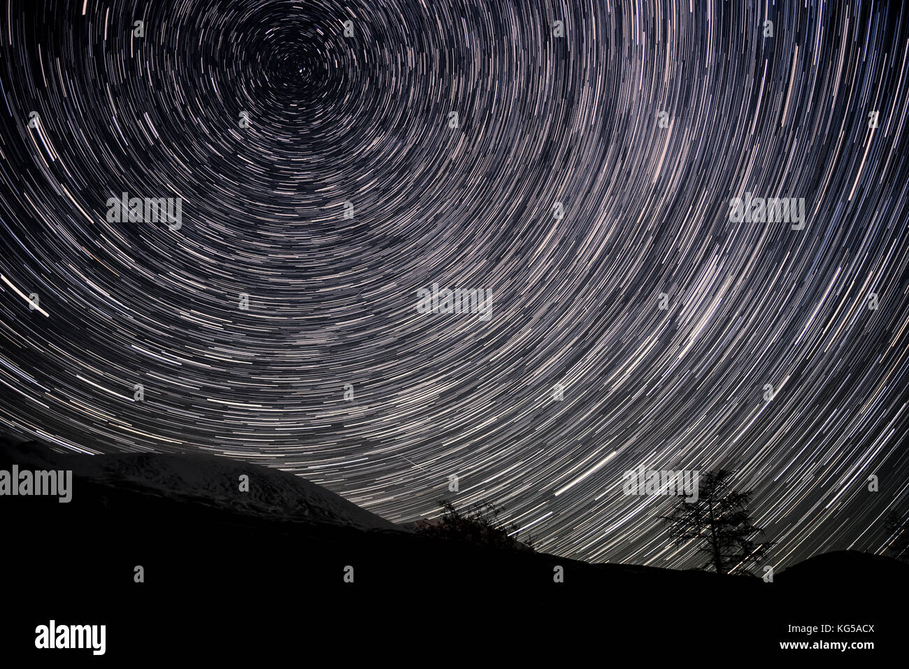 Belle Vue de nuit avec des traces d'étoiles tournant autour de l'étoile polaire, sous la forme de pistes circulaires sur fond de montagnes et d'arbres Banque D'Images