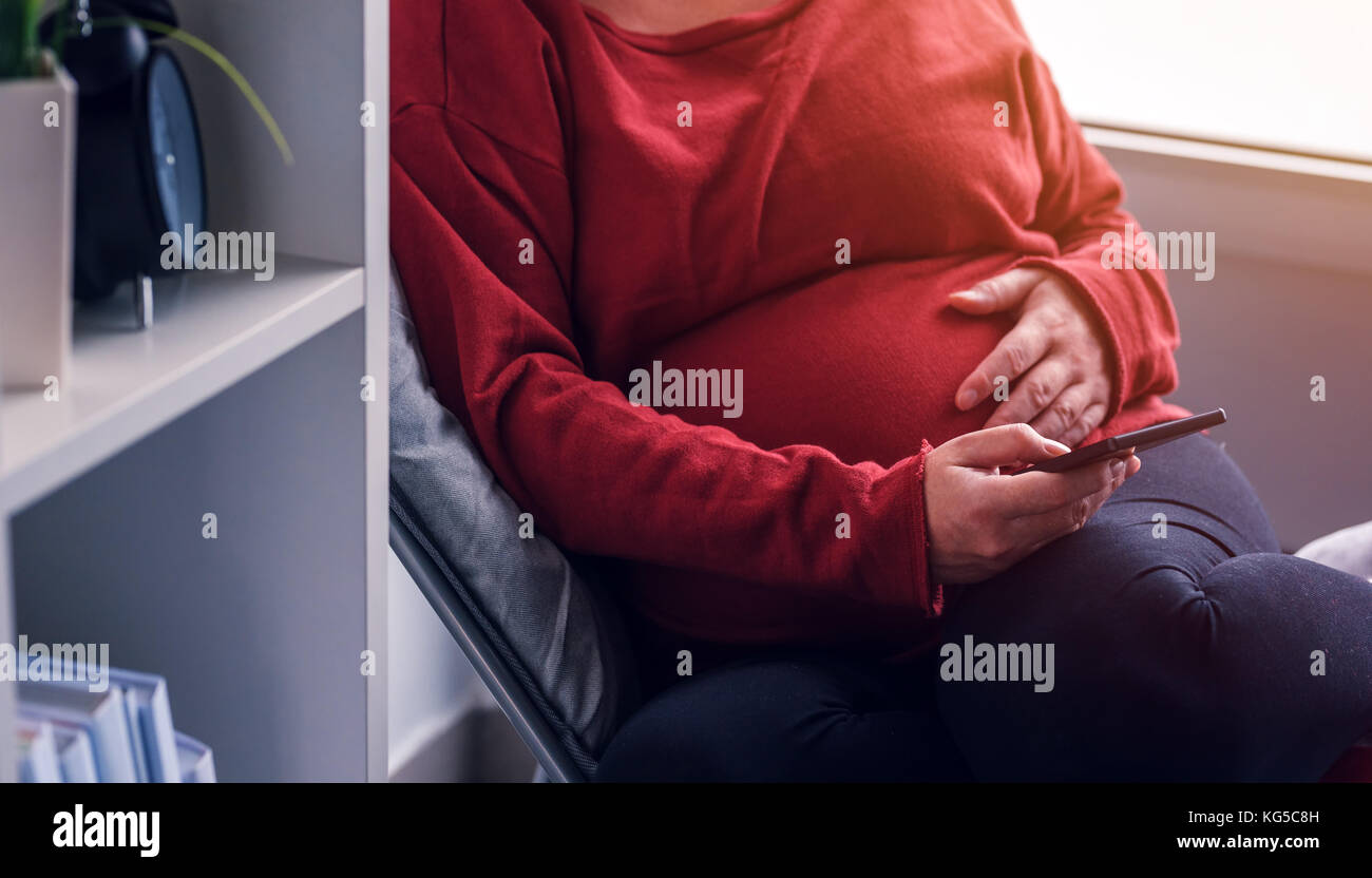 Femme enceinte détendue à l'aide de smart phone app mobile et à s'informer sur la grossesse et la maternité Banque D'Images