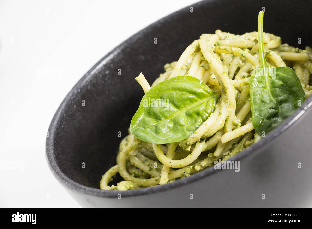 Les pâtes spaghetti avec sauce pesto dans le bol noir, gros plan sur fond blanc. Banque D'Images