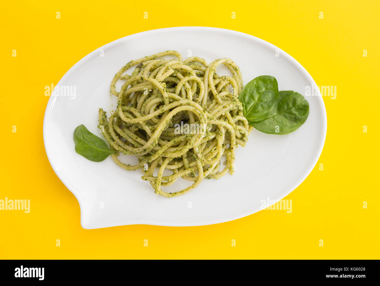 Les pâtes spaghetti au pesto dans un plat blanc en forme de chat bulle, sur fond jaune vif. Banque D'Images