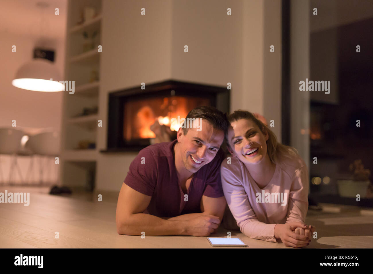 Jeune couple sur le sol en face de cheminée internet surf using digital tablet on nuit froide d'hiver Banque D'Images