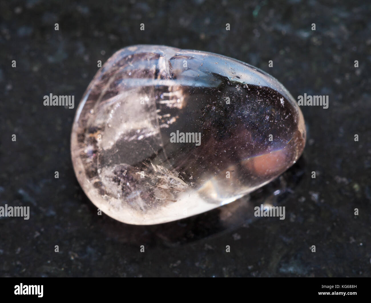 La prise de vue macro des eaux minérales naturelles rock specimen - tumbled quartz fumé gemstone sur fond de granit sombre Banque D'Images