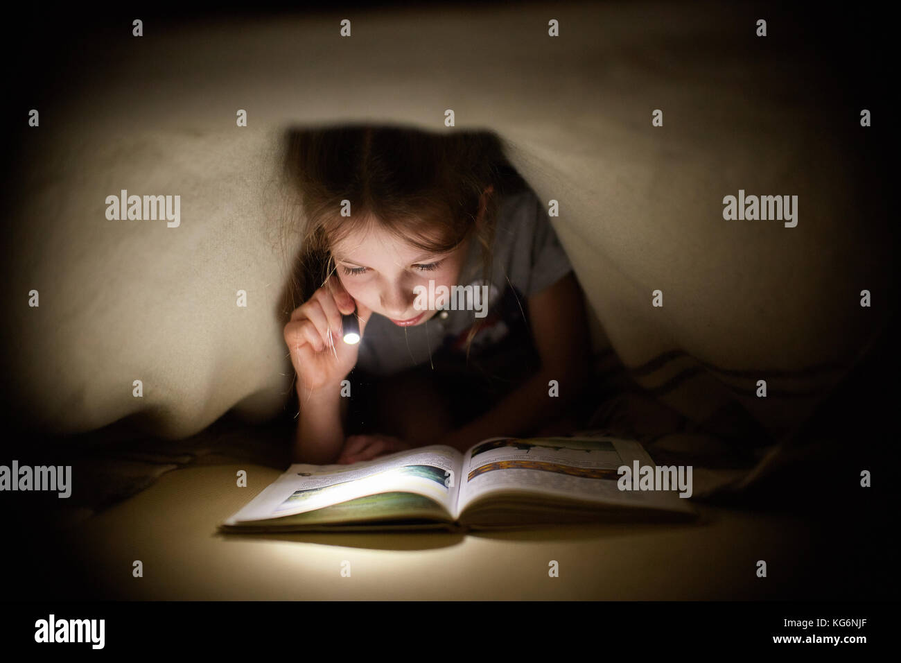 Petite fille est en train de lire un livre sous une couverture avec une  lampe de poche dans une pièce sombre dans la nuit Photo Stock - Alamy