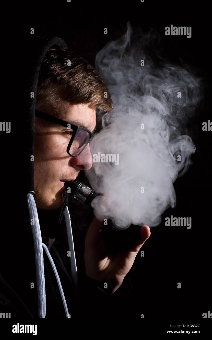 Jeune homme fume une cigarette électronique sur fond noir Banque D'Images