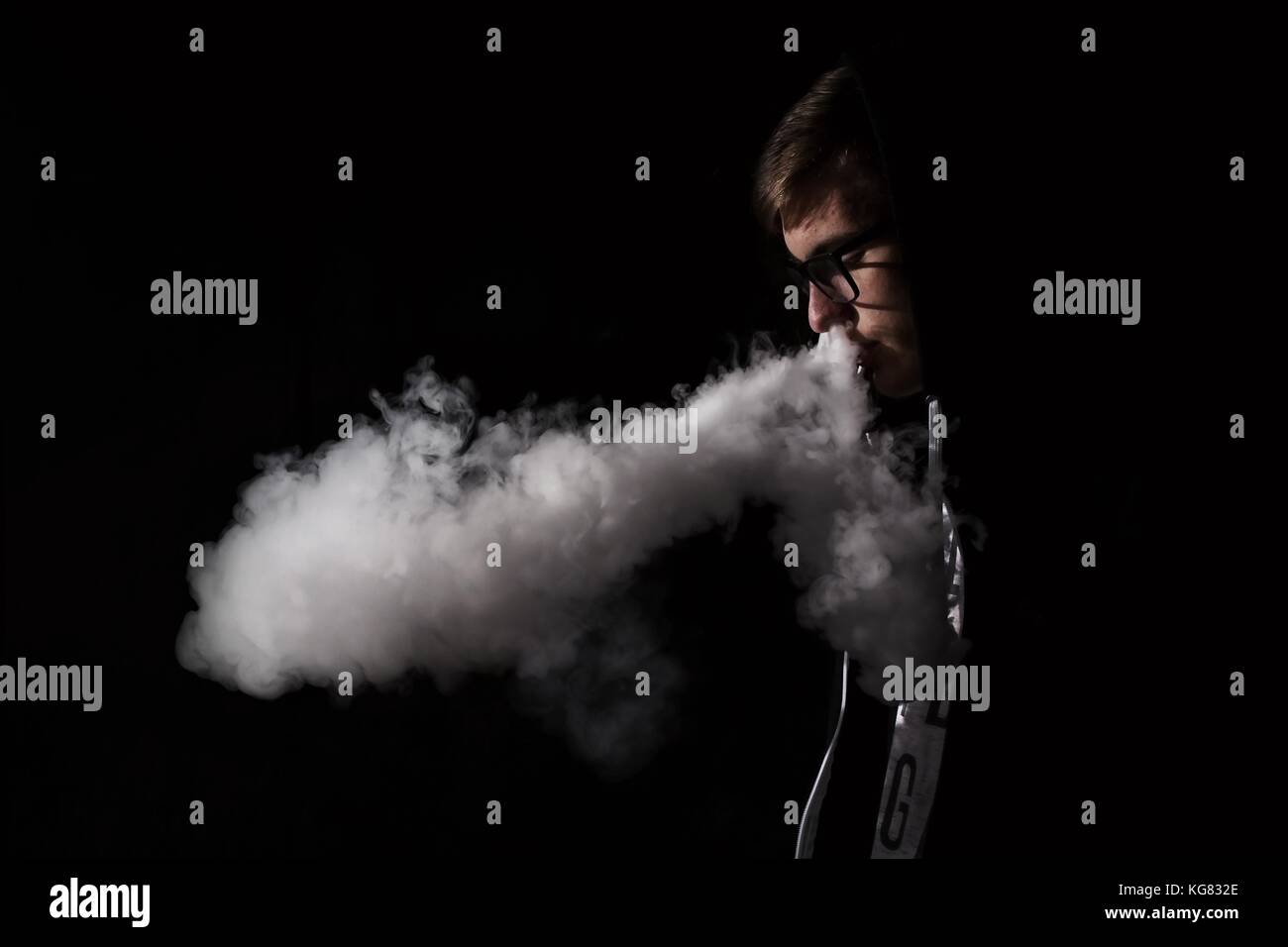 Jeune homme fume une cigarette électronique sur fond noir Banque D'Images
