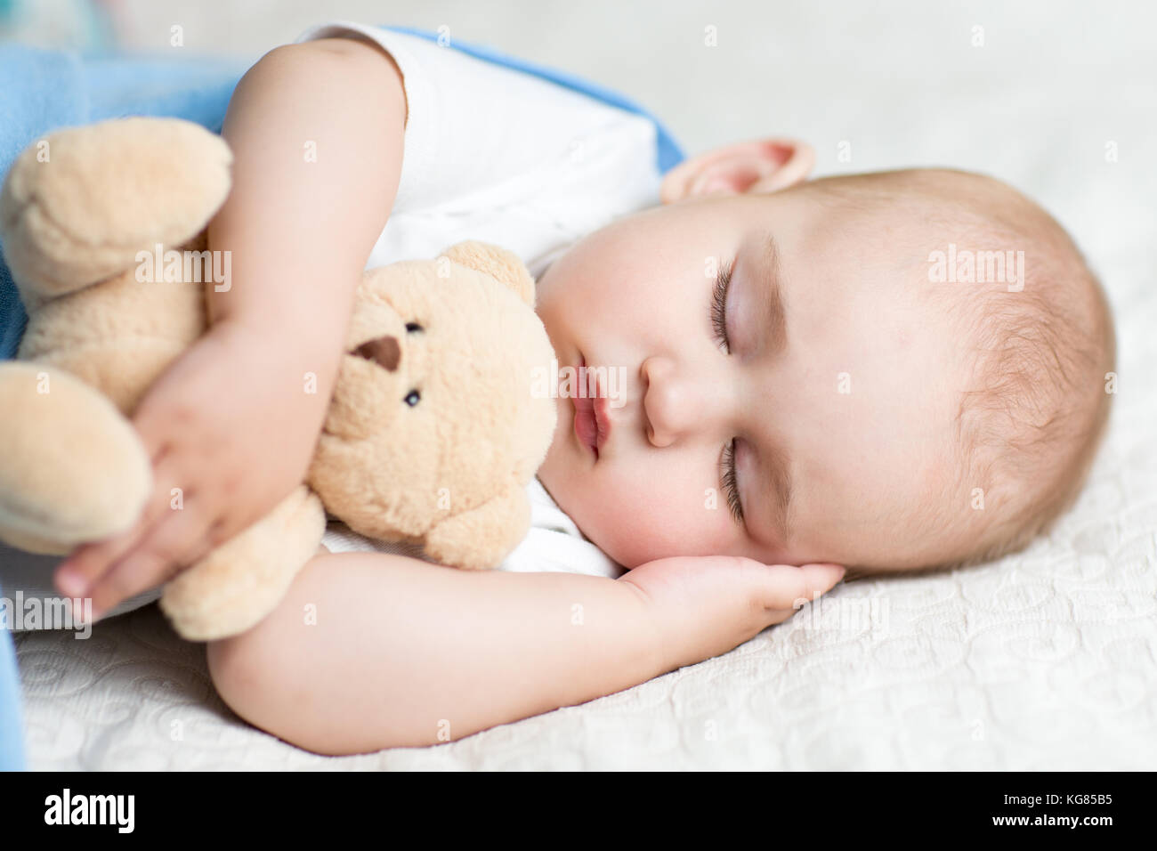 Bébé endormi dans son lit, tenant un ours en peluche. Banque D'Images