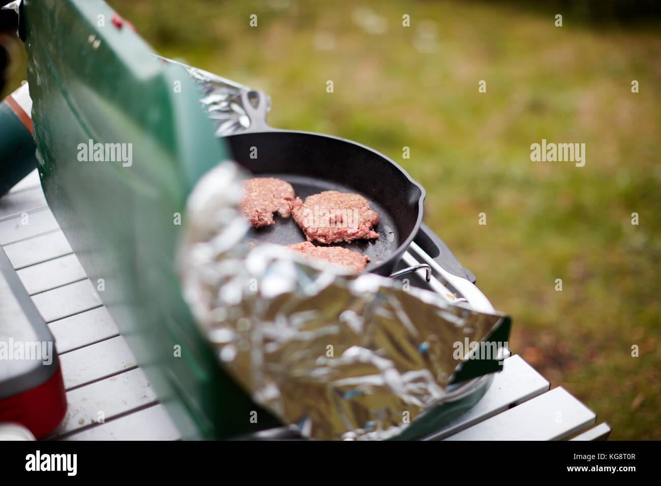 La cuisson des galettes sur un brûleur à gaz en plein air avec des gardes du vent d'aluminium mis en place sur une petite table portable en camping Banque D'Images