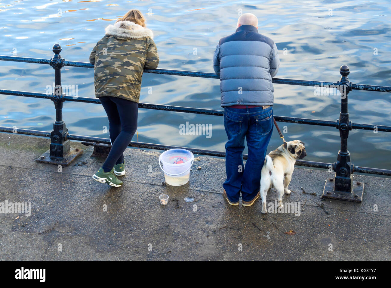 Un couple avec un chien pug la pêche de crabes de Whitby Harbour sur une journée ensoleillée d'automne Banque D'Images