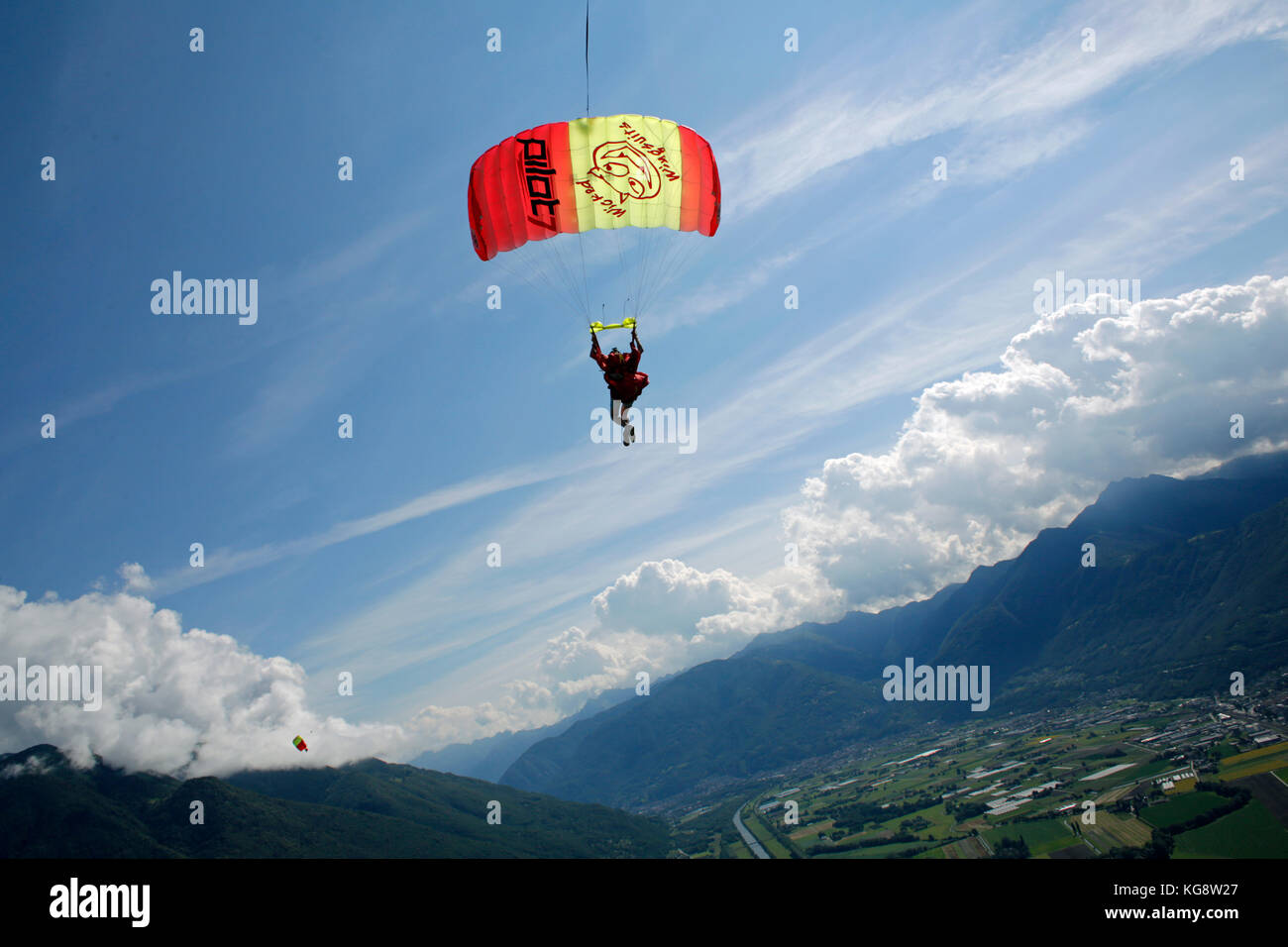 Parachutiste est volant sous son parachute et d'aller à terre sur l'herbe verte. Il est ainsi le ralentissement de l'auvent en tirant les pauses. Banque D'Images