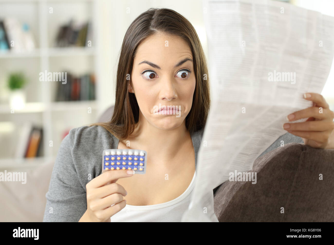 Portrait d'une jeune fille confus lecture contre-indications dans une brochure de pilules contraceptives assis sur un canapé dans un intérieur de la chambre Banque D'Images