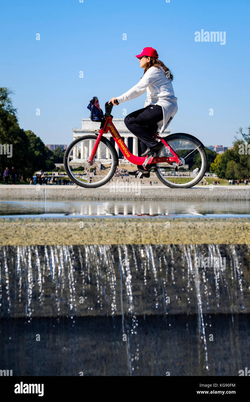 Cycliste féminine équitation un capital Bikeshare location avec l'Abraham Lincoln Memorial en arrière-plan, Washington, DC, United States of America, USA. Banque D'Images