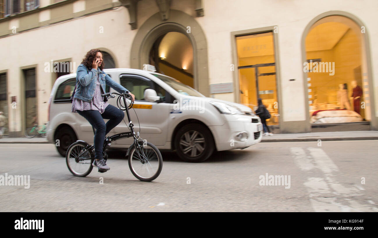 Femme locale chevauchant dans les rues de Florence sur un vélo pliant tout en parlant sur son téléphone portable Banque D'Images