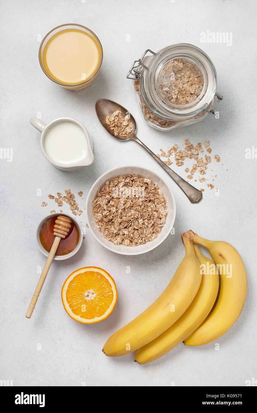 Ingrédients pour le petit déjeuner : céréales, lait, miel, orange, jus d'orange, les bananes sur un fond blanc en béton. Vue de dessus Banque D'Images