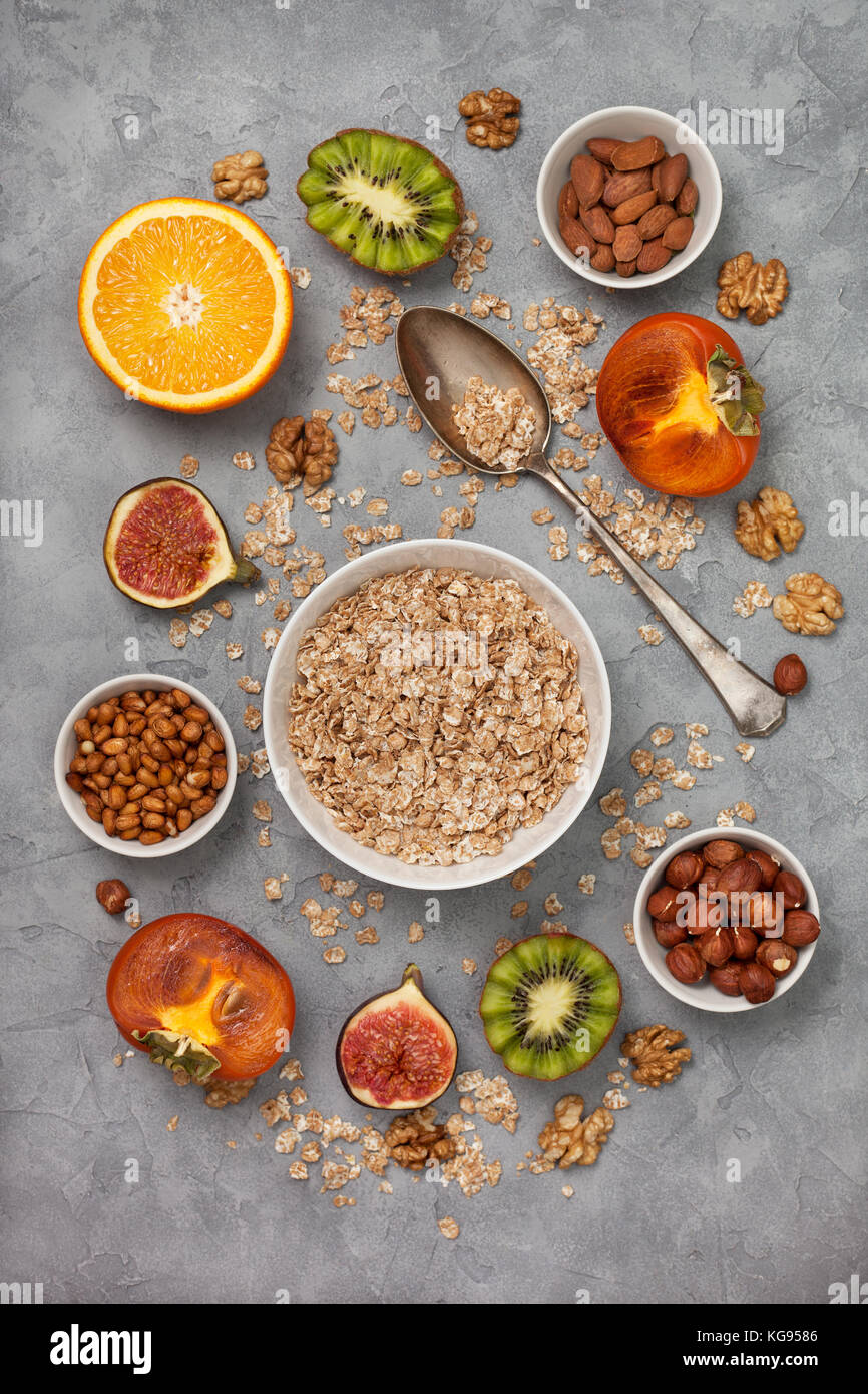 Petit-déjeuner sain : muesli et fruits frais : orange, kaki, fig, kiwi et noix sur une base de béton gris. Vue de dessus Banque D'Images