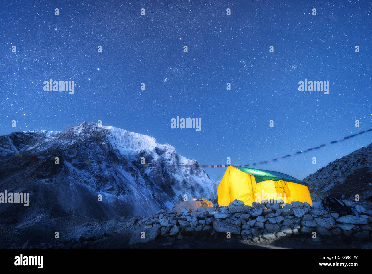 Brillant jaune tente contre de hautes roches avec pic enneigé et le ciel avec des étoiles la nuit au Népal. Les montagnes de l'himalaya. Paysage avec montagnes, ciel étoilé Banque D'Images