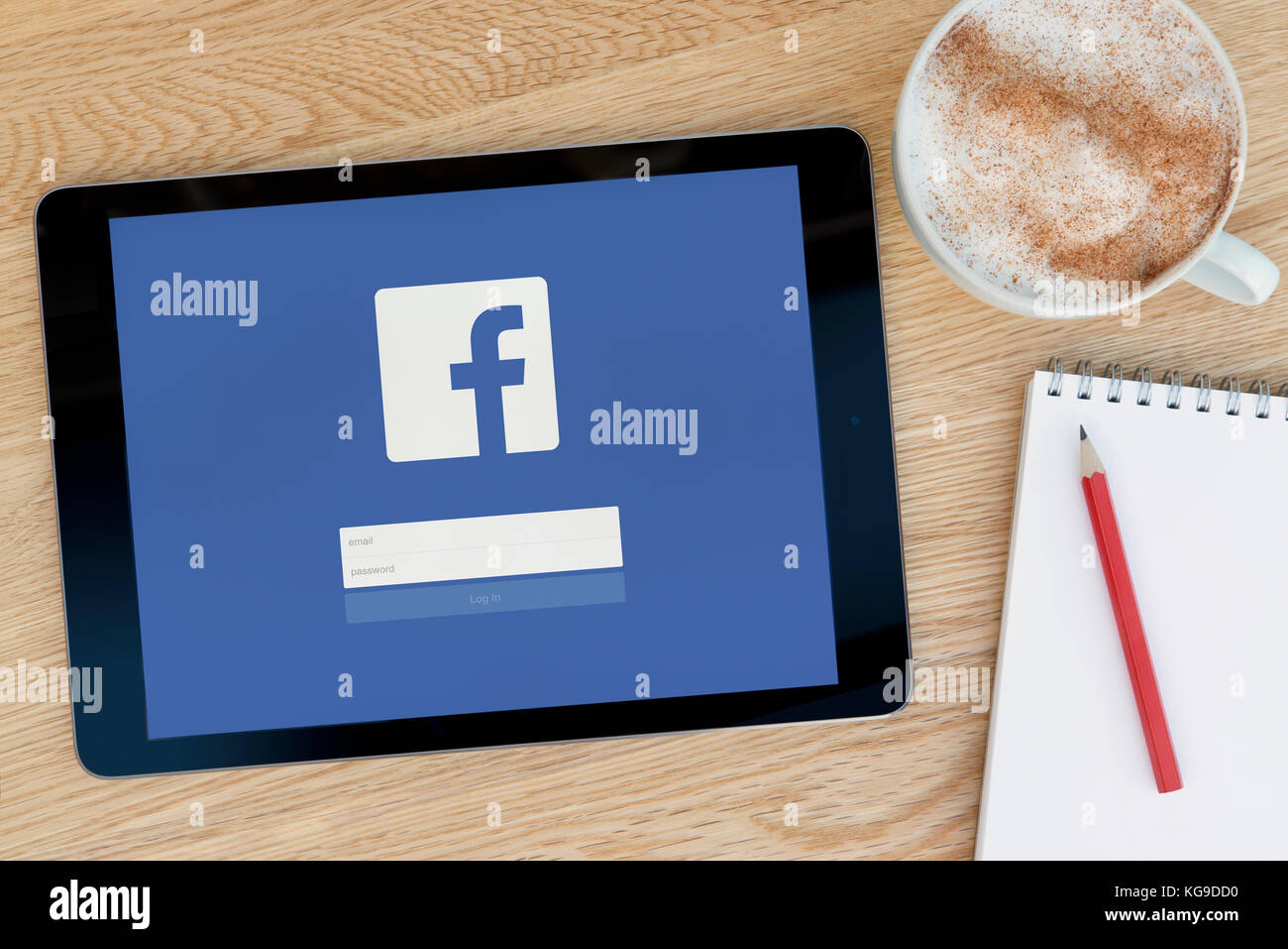 Le site Facebook fonctionnalités sur un iPad tablet device qui repose sur une table en bois à côté d'un bloc-notes et un crayon et une tasse de café (rédaction uniquement) Banque D'Images