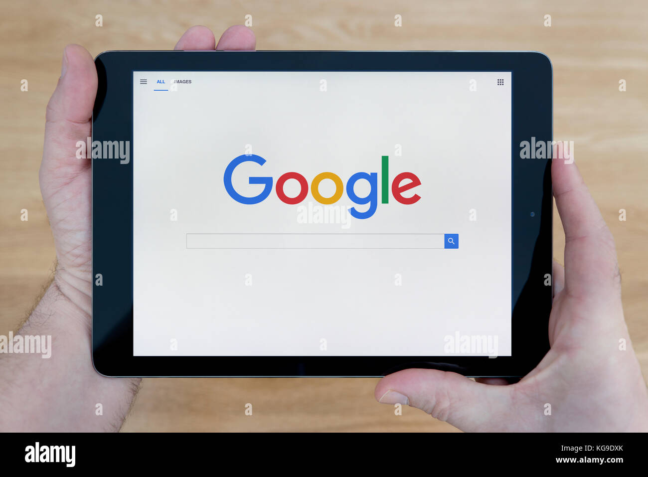 Un homme regarde le site web de Google sur son iPad tablet device, tourné contre une table en bois page contexte (usage éditorial uniquement) Banque D'Images