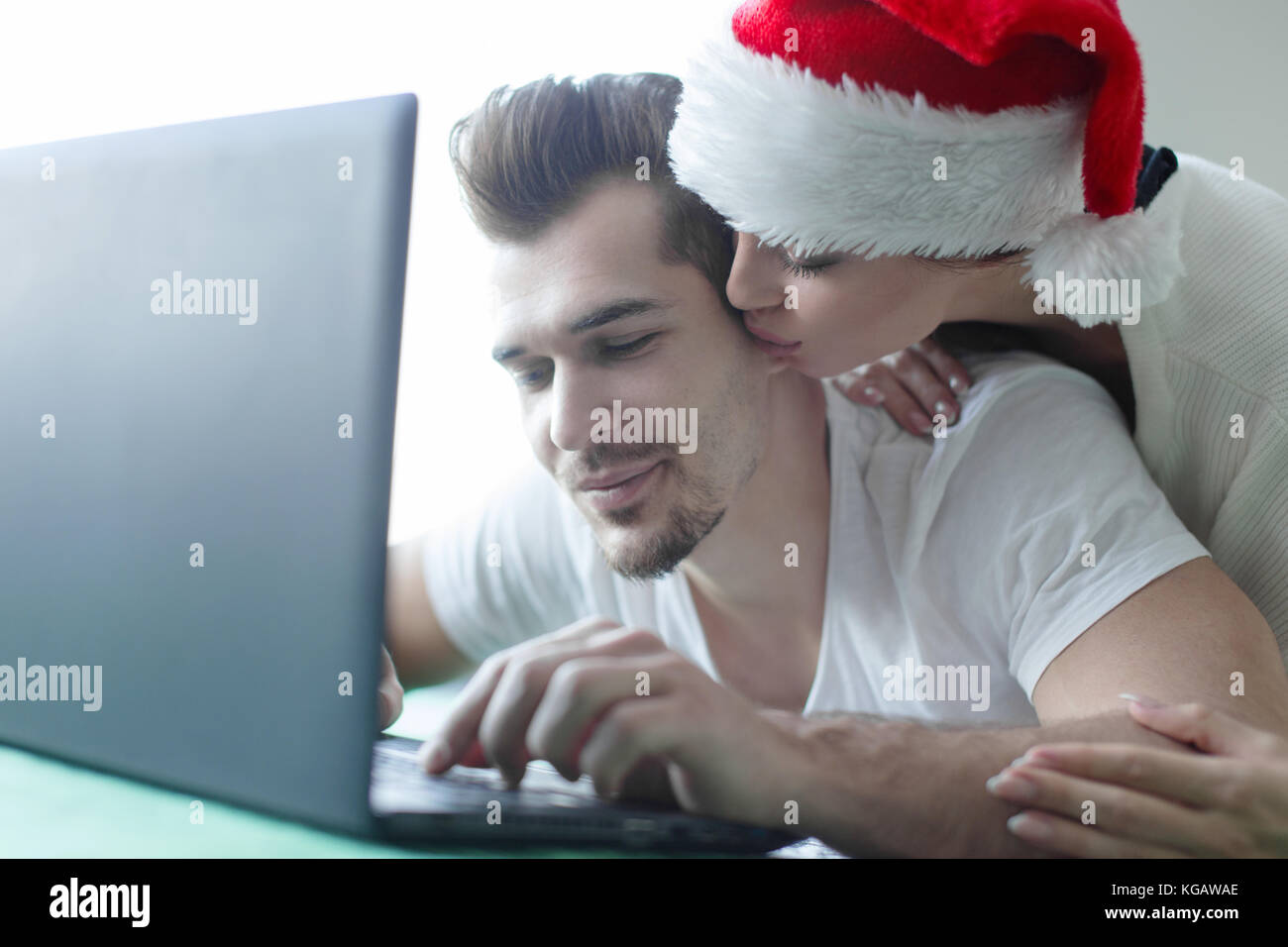 Jeune couple magasinage en ligne par l'ordinateur portable à la maison pour Noël petite amie hug Banque D'Images