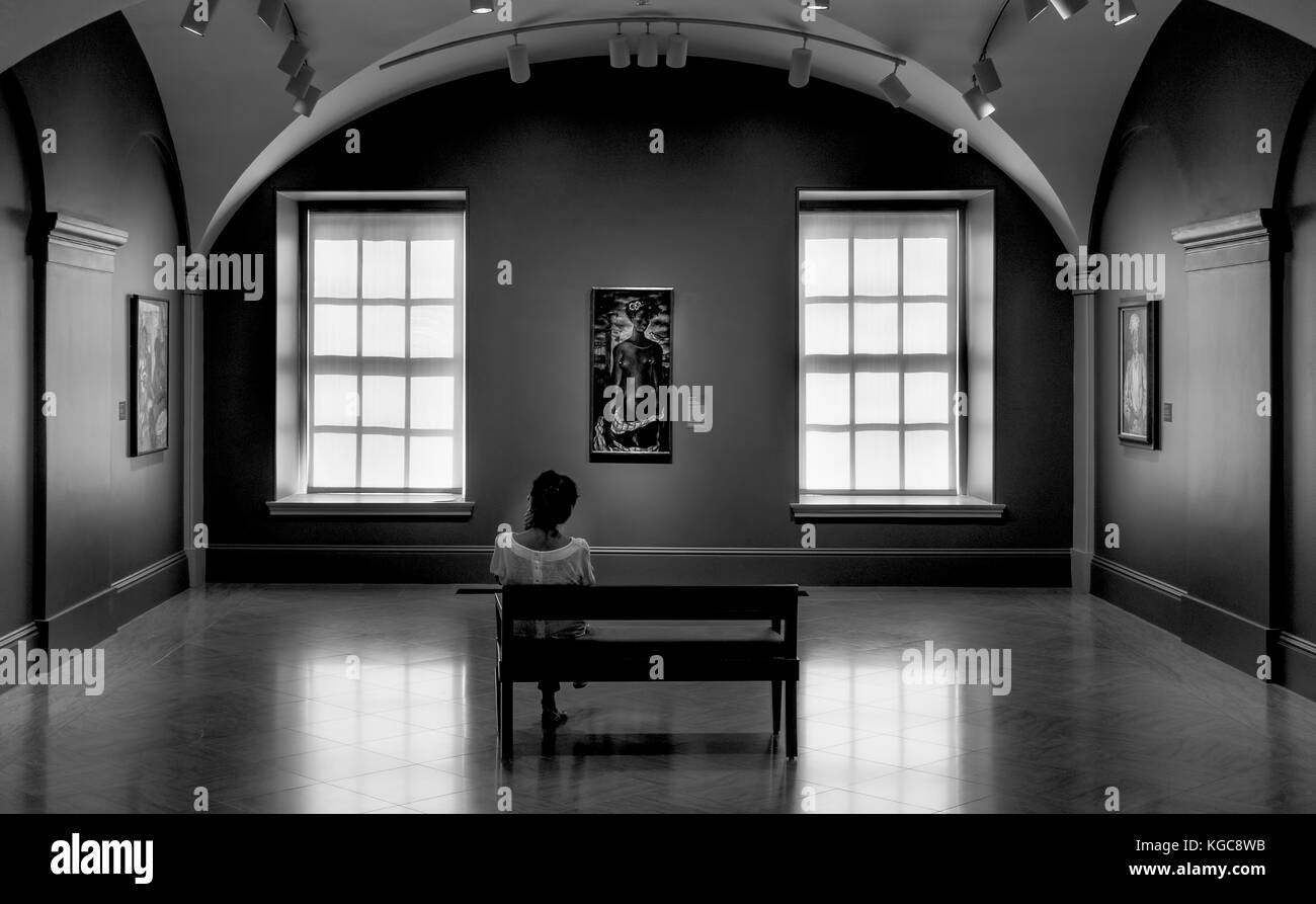 Une femme assise sur un banc en contemplant une peinture au musée en noir et blanc. elle est seule avec ses pensées. Banque D'Images