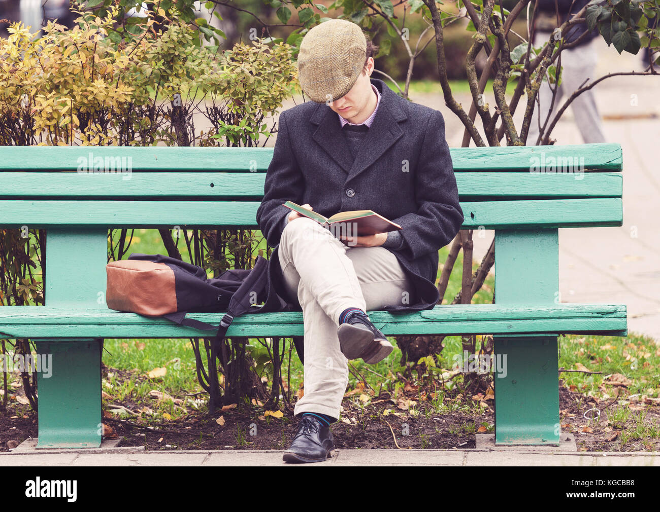 Jeune homme assis sur le banc dans un parc et la lecture d'un livre à Vilnius, Lituanie Banque D'Images