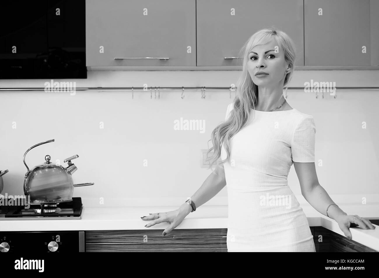 Photo en noir et blanc de jeune fille blonde à la caméra dans la cuisine Banque D'Images