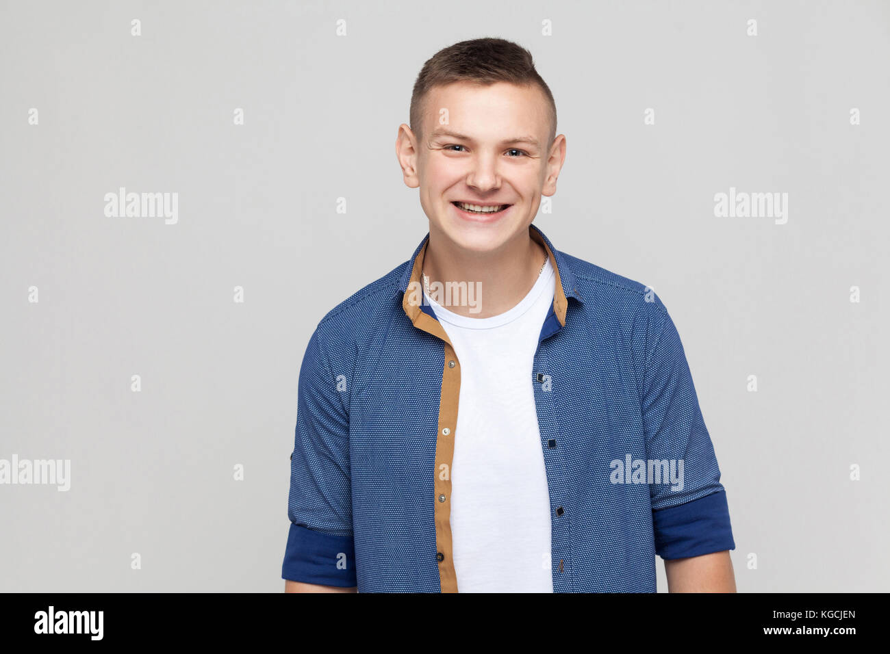Jeune homme portant succès chemise bleue à la caméra et à sourire à pleines dents. studio shot, fond gris Banque D'Images