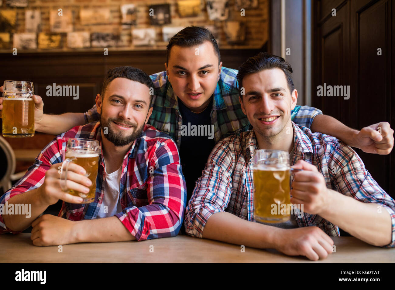 Trois jeunes hommes sont souriants et qui retentit verres de bière ensemble tout en restant assis dans un pub Banque D'Images