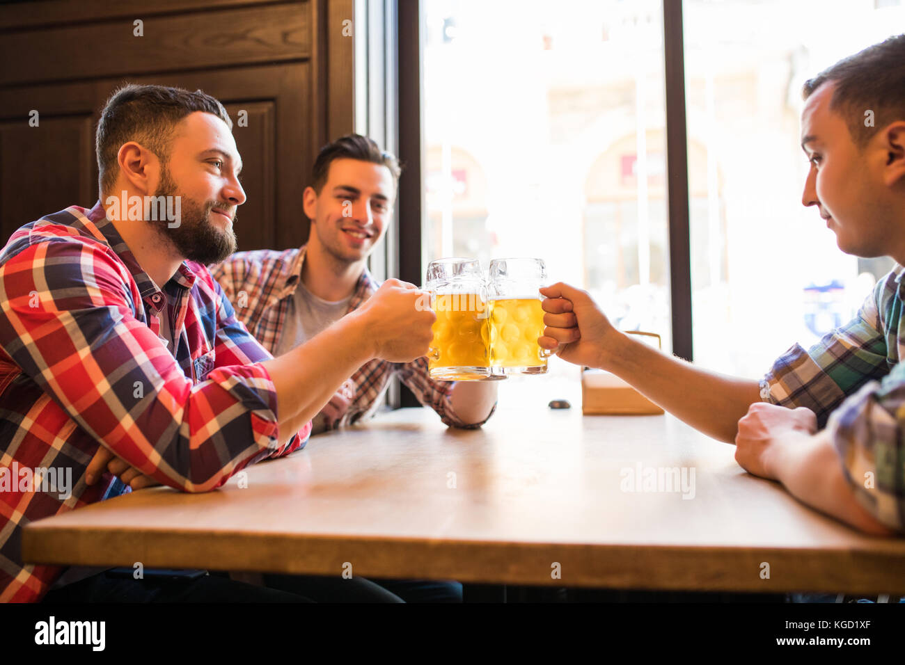Trois jeunes hommes sont souriants et qui retentit verres de bière ensemble tout en restant assis dans un pub Banque D'Images