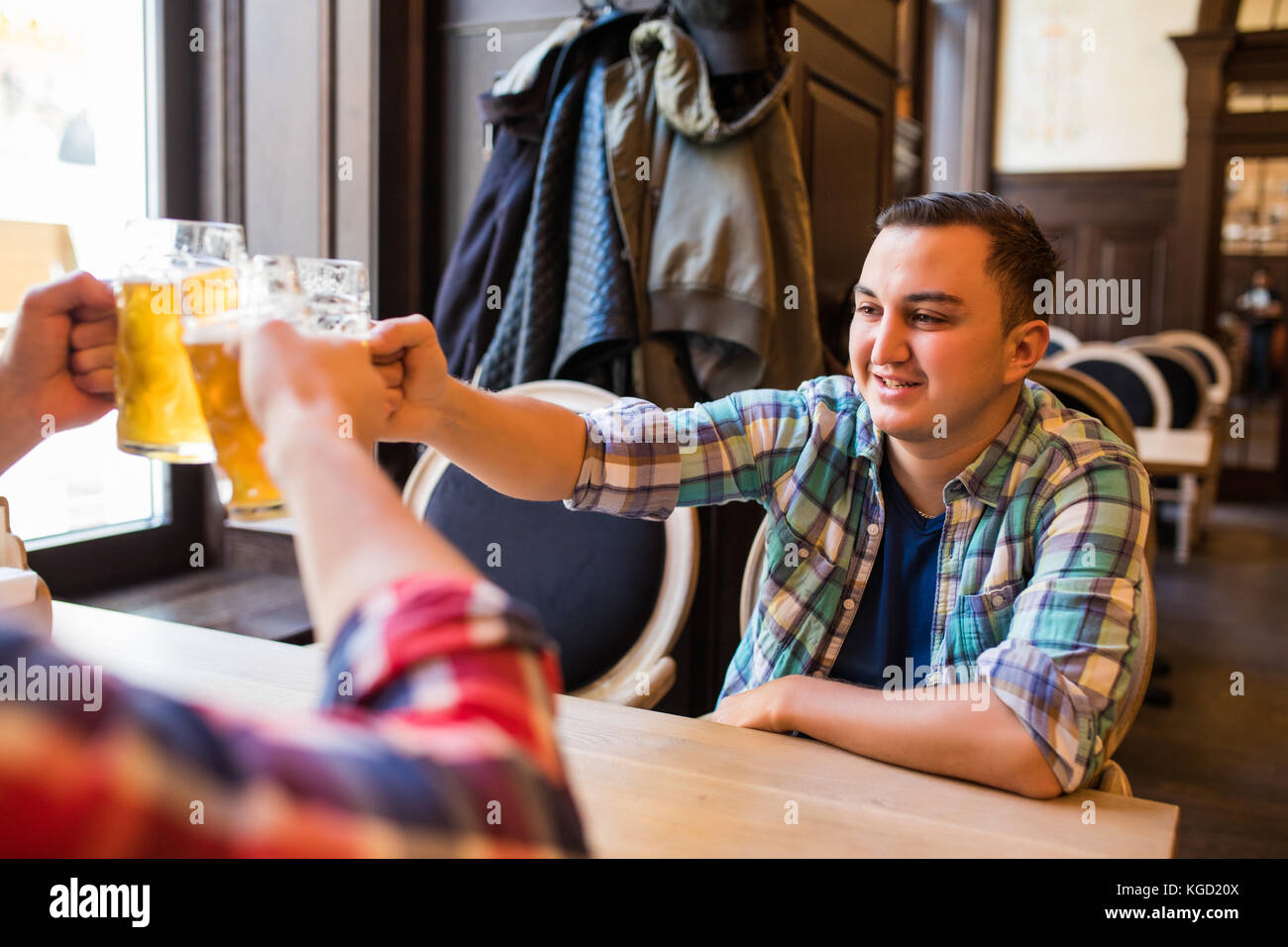Trois jeunes hommes en vêtements décontractés sont souriants qui retentit et verres de bière ensemble tout en restant assis dans un pub Banque D'Images