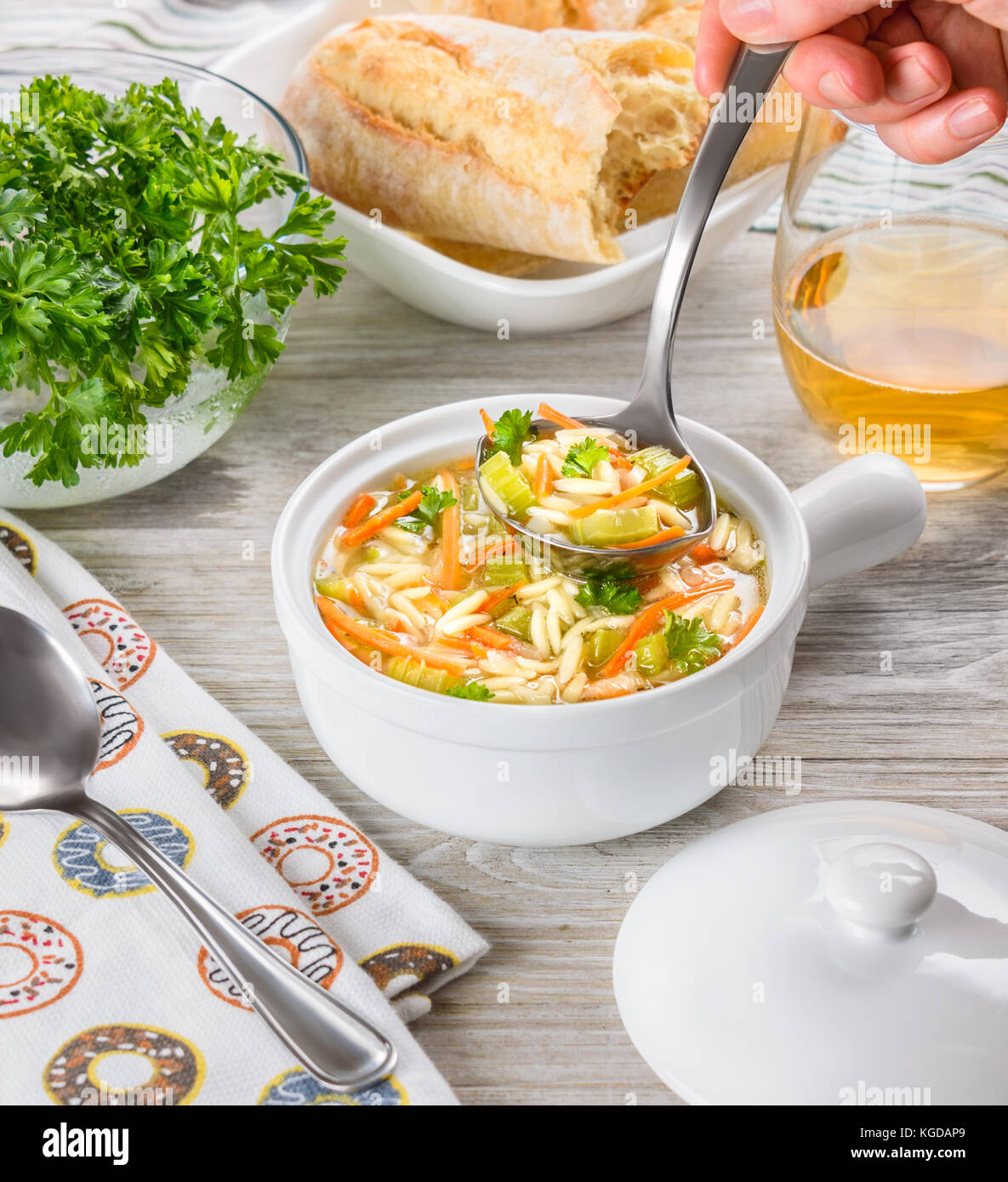Soupe de poulet l'orzo dans une cruche blanche sur fond de bois. L'italien orzo de soupe avec du chef. main tenant une louche. Pain. verre de vin. Banque D'Images
