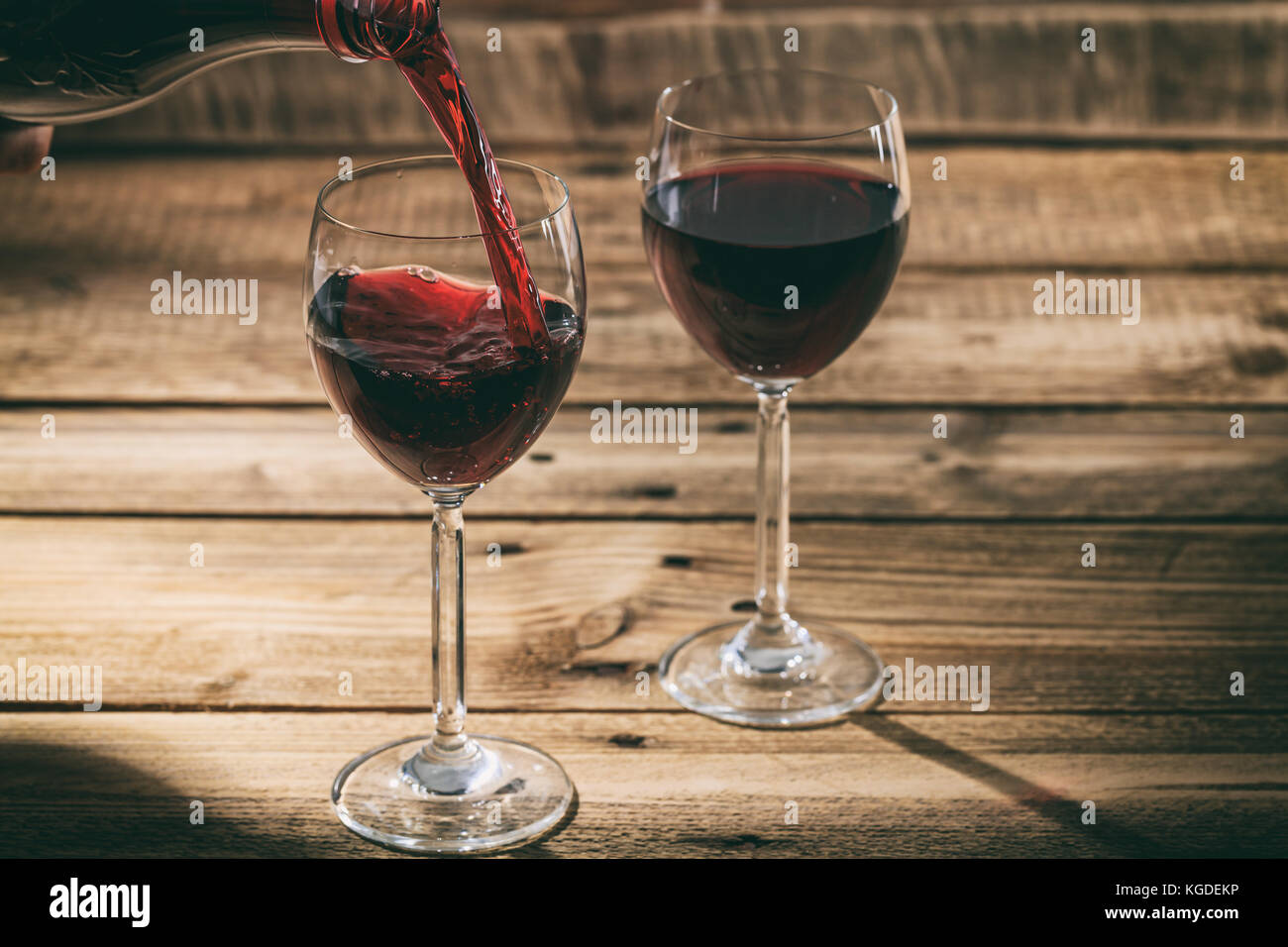 Verser le vin rouge dans un verre sur une table en bois Banque D'Images