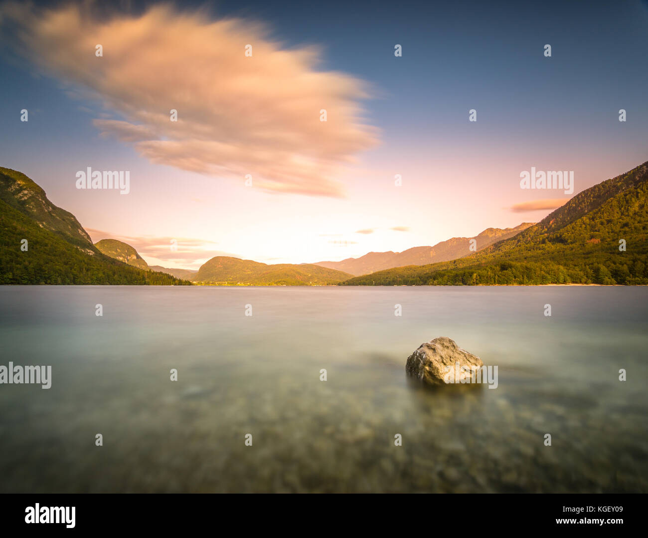 Une longue exposition rock dans le lac au coucher du soleil plage de galets avec la lumière. Banque D'Images