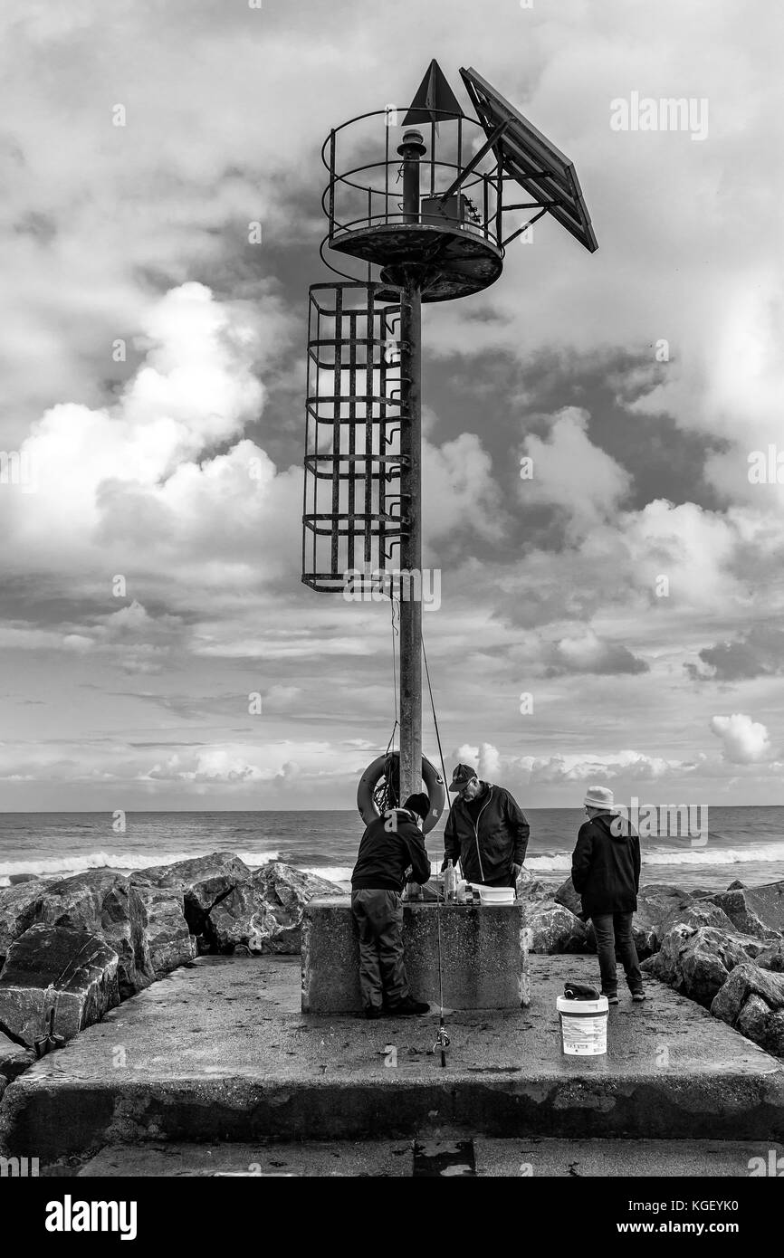 Trois personnes pêchant une journée nuageux au bord de la mer Banque D'Images