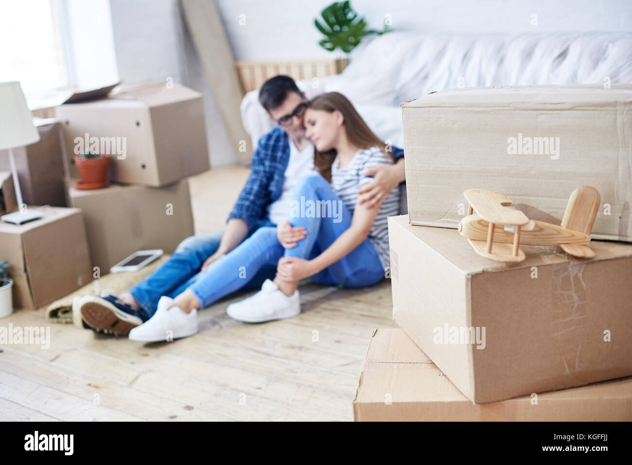 Beau jeune homme embrassant sa jolie petite amie tout en étant assis sur le plancher du nouvel appartement et à rêver de leur cohabitation, des piles de déménagement boxe Banque D'Images