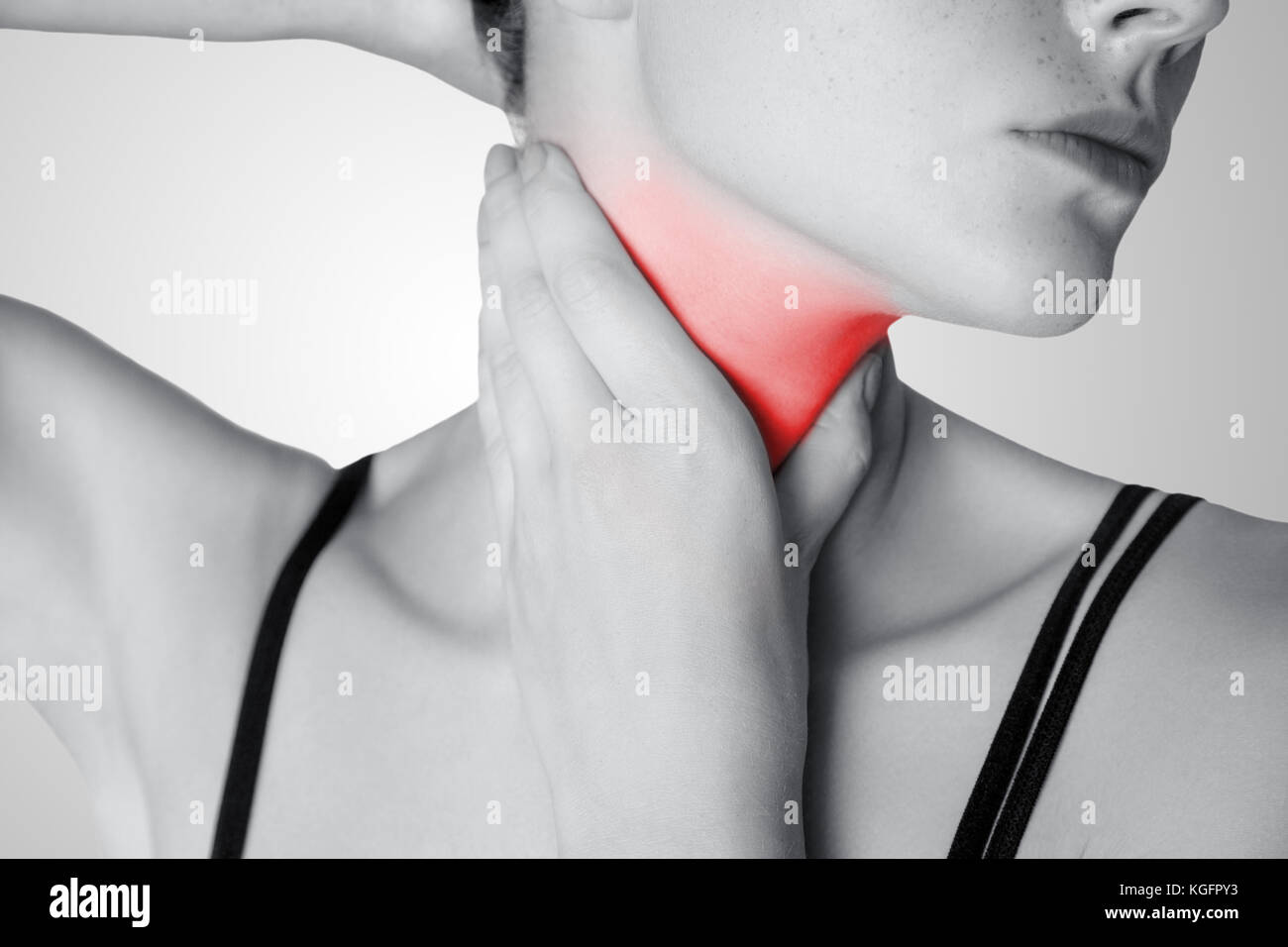 Vue rapprochée d'une jeune femme avec la douleur sur le cou ou glande thyroïde sur fond gris. noir et blanc avec un point rouge. Banque D'Images