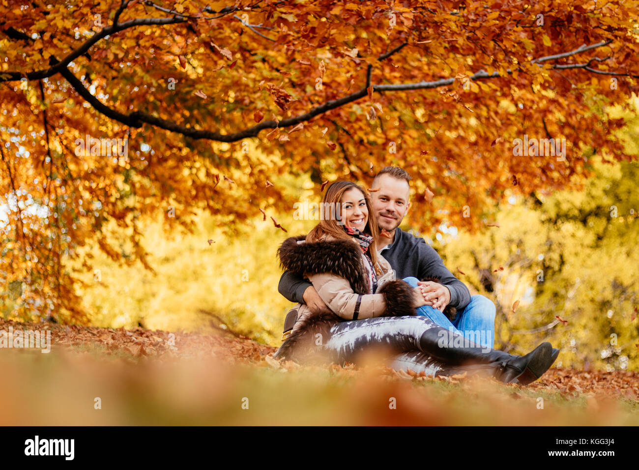 Beautiful smiling couple enjoying sunny forêt en automne couleurs. Ils sont assis sur la tombe des feuilles et à la recherche à l'appareil photo. Banque D'Images