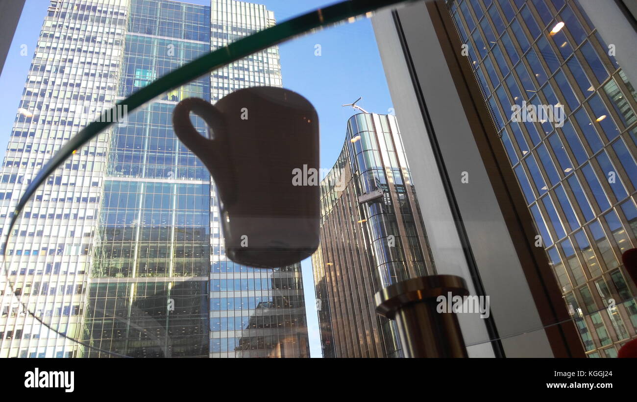 Une tasse de café sur une table en verre qui reflètent un gratte-ciel à Canary Wharf, Londres. Banque D'Images