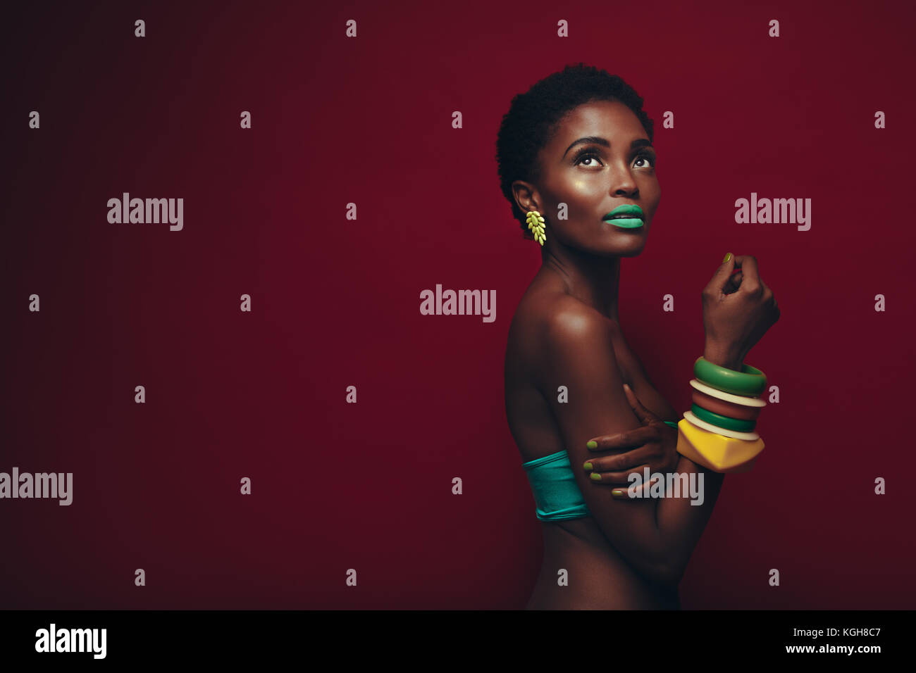 Jolie jeune femme africaine avec de maquillage. Portrait of female model aux couleurs maquillage sur fond rouge. Banque D'Images