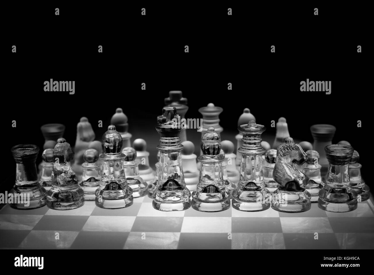 Photo noir et blanc de la planche d'échecs et des pièces d'échecs en verre transparent, fond noir. Banque D'Images