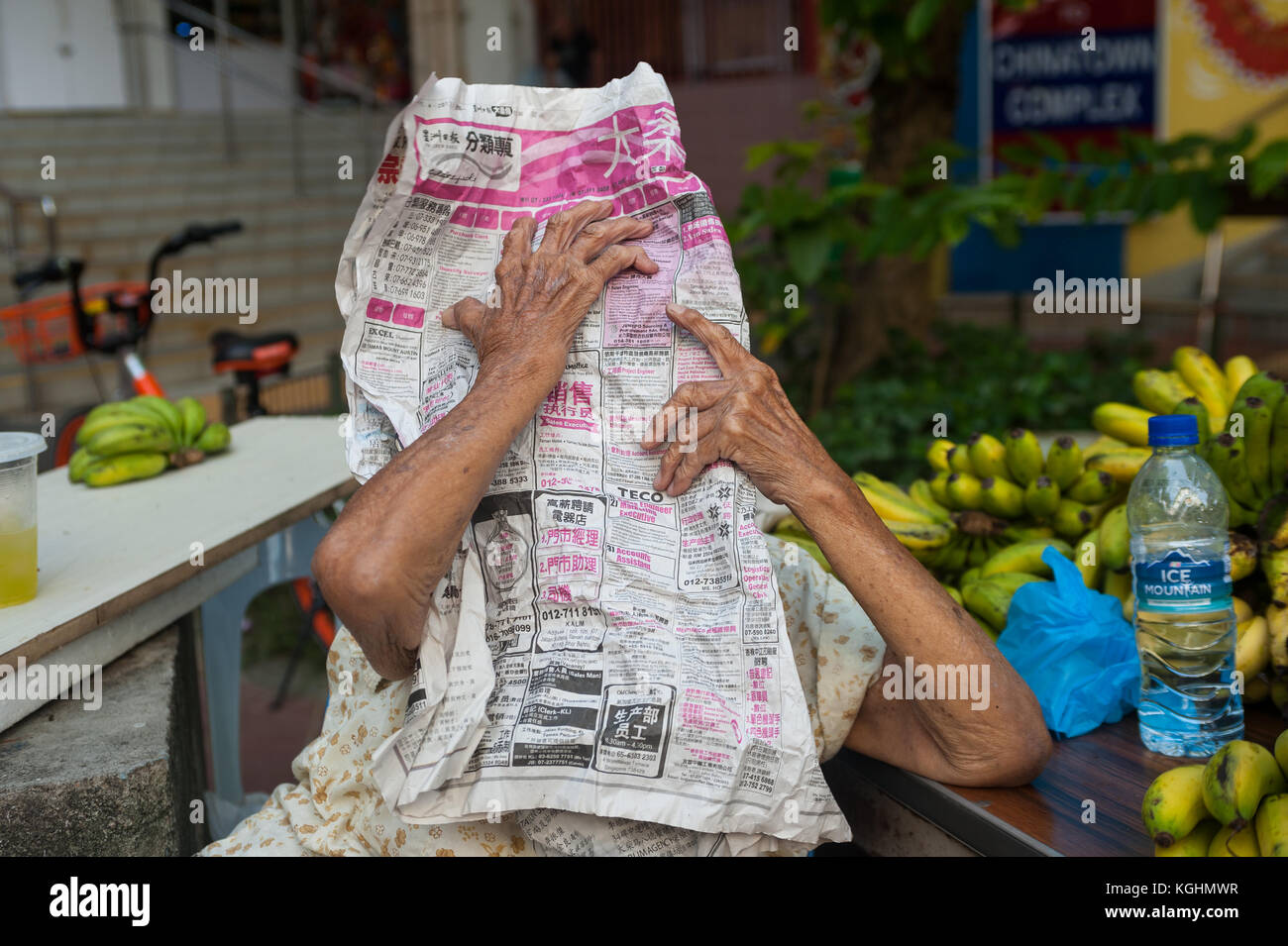 03.11.2017, Singapour, République de Singapour, en Asie - une vieille femme qui vend des bananes dans le quartier de Chinatown à Singapour se cache derrière un journal. Banque D'Images