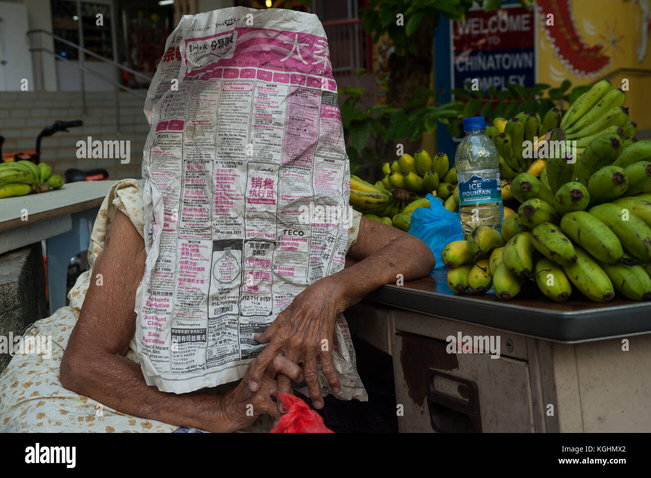 03.11.2017, Singapour, République de Singapour, en Asie - une vieille femme qui vend des bananes dans le quartier de Chinatown à Singapour se cache derrière un journal. Banque D'Images