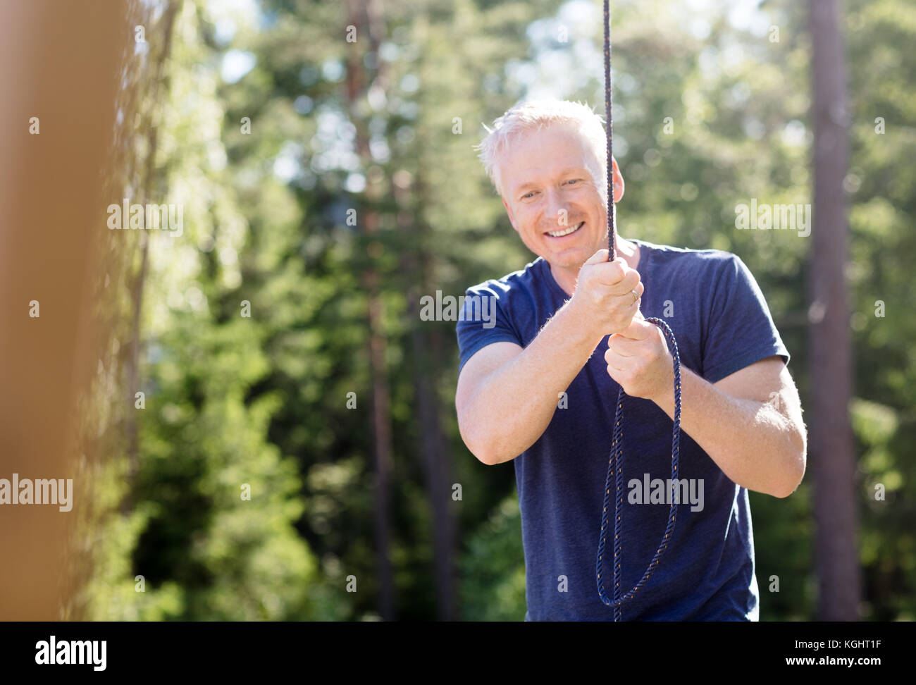 Man smiling while holding rope in forest Banque D'Images
