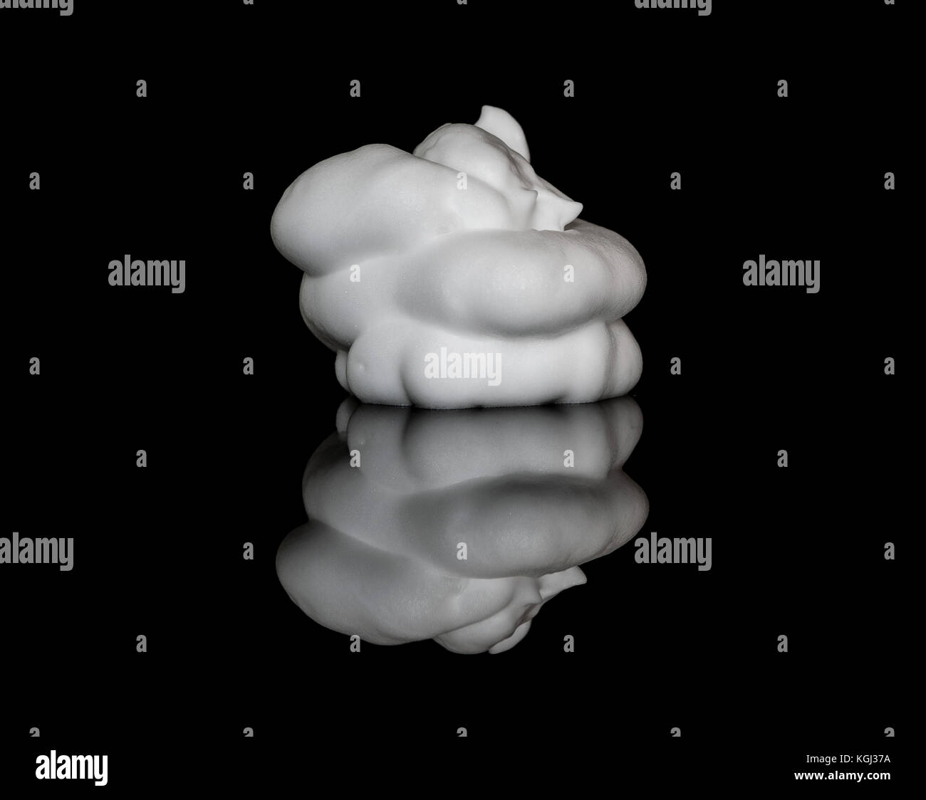 Mousse à raser mousse blanche sur le dessus d'une surface en verre réfléchissant noir, isolé sur fond noir Banque D'Images
