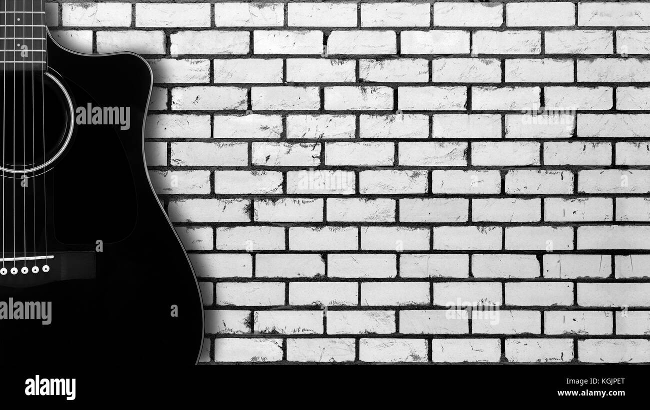 Instrument de musique - silhouette d'une guitare acoustique noire avec pan coupé sur un mur en brique blanche arrière-plan. Banque D'Images