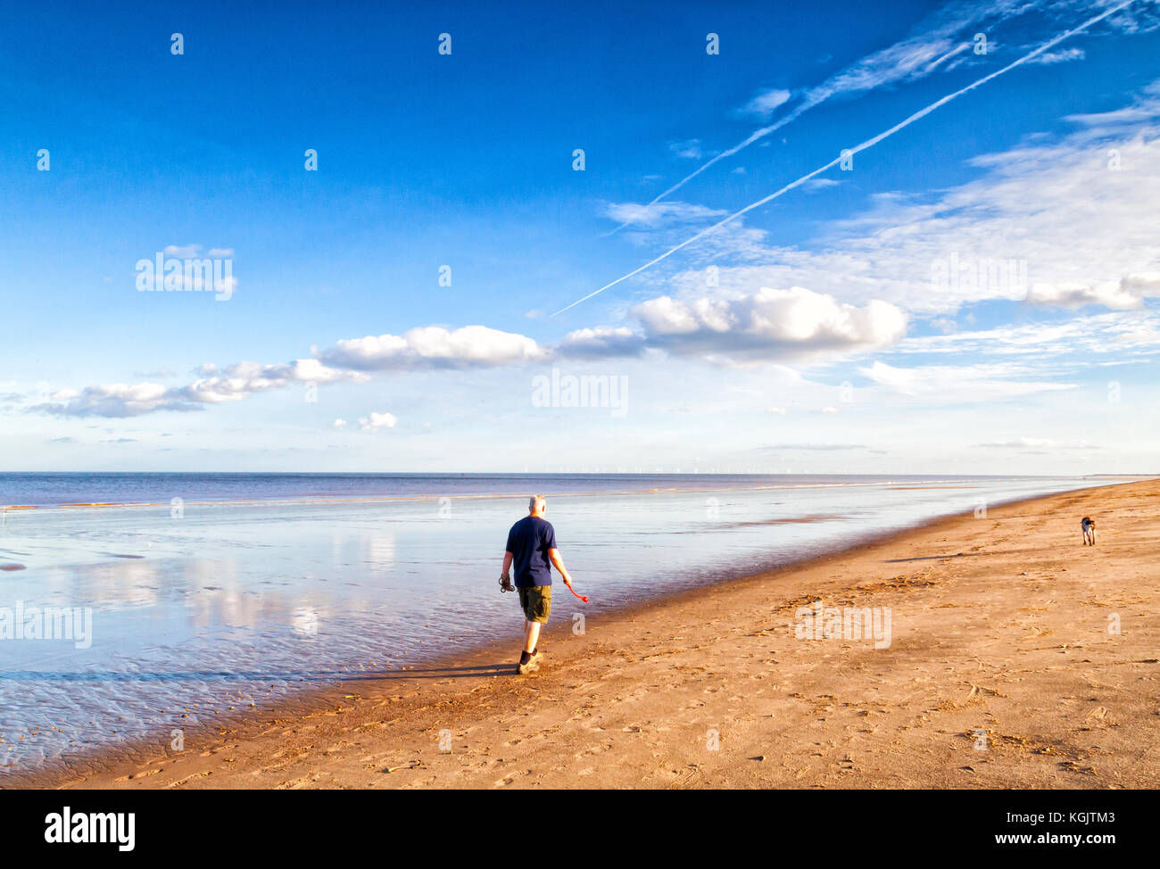 Man Walking on beach with dog in distance, sur la côte est d'angleterre Banque D'Images