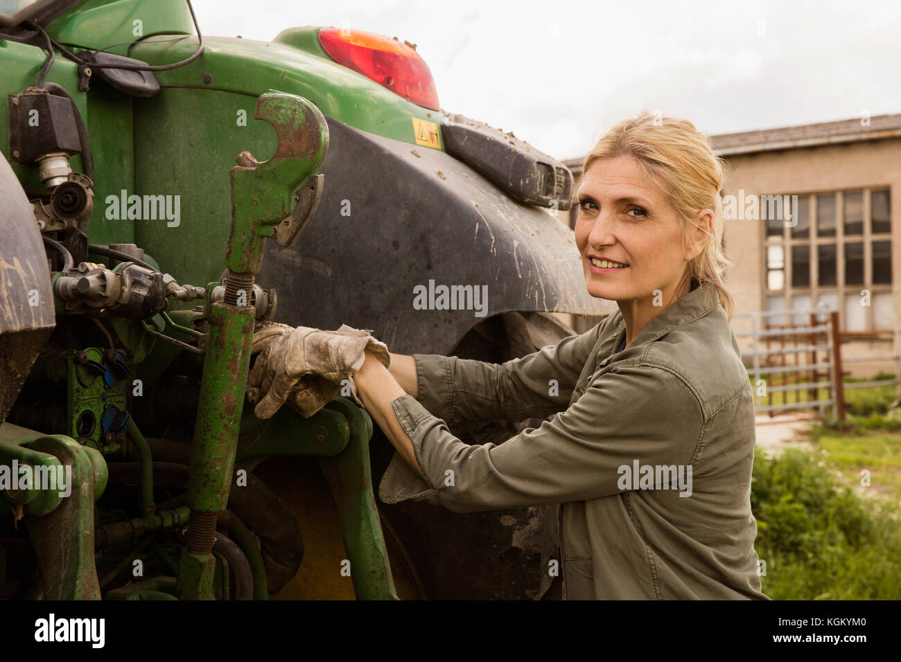 Portrait of smiling female farmer standing par la machinerie agricole contre le ciel Banque D'Images