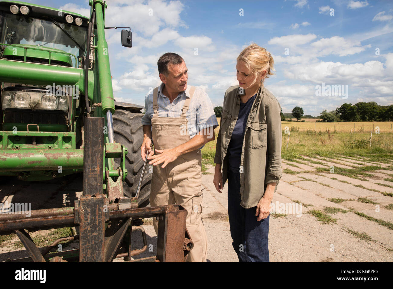 Homme Femme expliquant tout en se tenant par les machines agricoles à la ferme Banque D'Images
