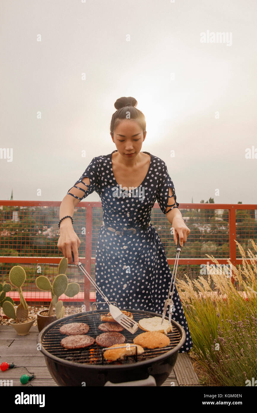 Jeune femme au barbecue steak et des brioches au patio contre ciel clair Banque D'Images