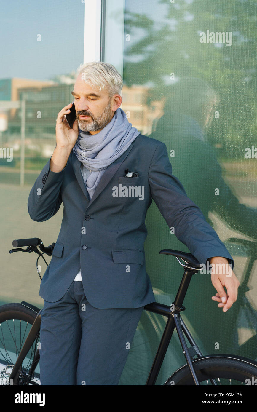 Businessman with bicycle talking on mobile phone debout contre l'édifice de verre Banque D'Images