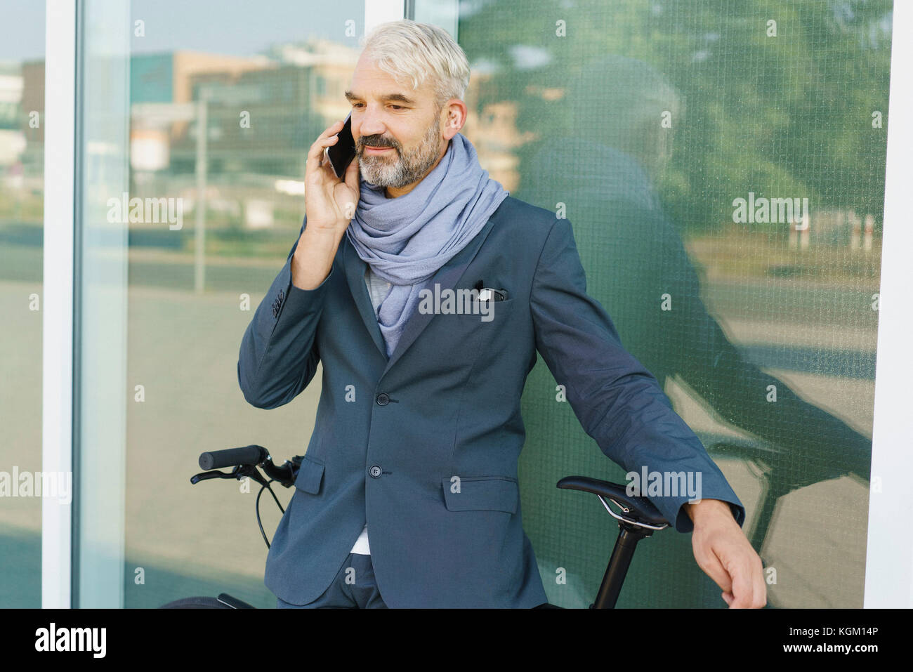 Confident businessman with bicycle talking on mobile phone debout contre l'édifice de verre Banque D'Images